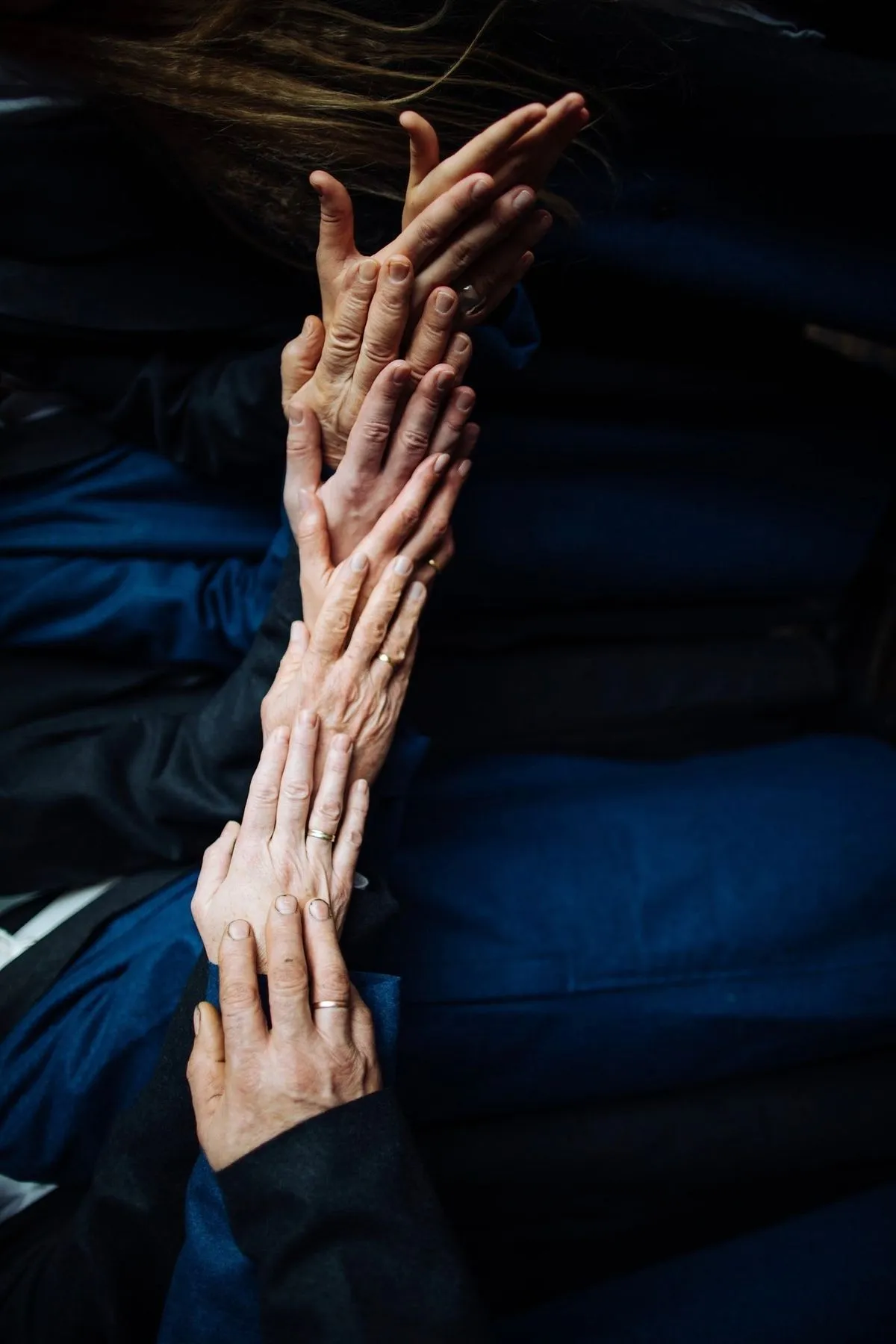 Several hands reaching upward together against dark blue fabric